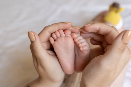 Unrecognizable mother holding tiny feet of her newborn baby daughter or sonの写真素材