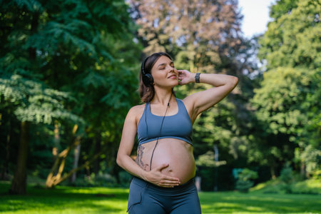 Pregnant woman with headphones listening music during yoga workout in park