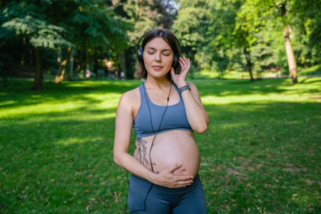 Sporty pregnant woman with headphones after sport workout in park
