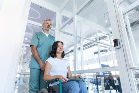 Male doctor carrying a wheelchair with a female patient in the hospital corridorの写真素材