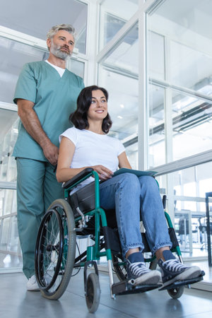 Male doctor assisting a female patient in a wheelchair in the hospital corridorの写真素材