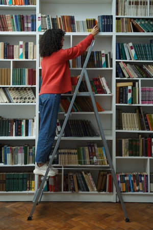 Curly-haired young girl in red jacket on the ladder in the library