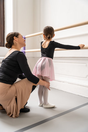 Ballerina teaching young beginner in ballet class helping her practice poses and balance at barreの写真素材