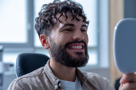 Man in dental clinic using mirror to examine his teeth providing orthodontic treatmentの写真素材