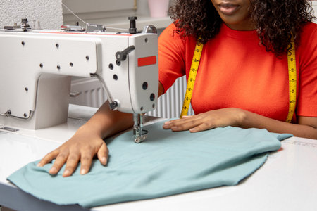 African american dressmaker sitting at the sewing machine and looking contented