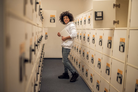 Curly-haired young guy standing near the lockers in library archive