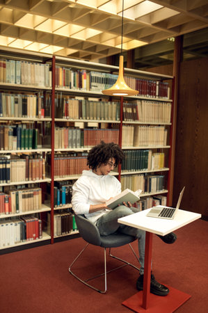Curly-haired young man studying in the library and looking involved