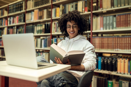 Curly-haired young man studying in the library and looking involved