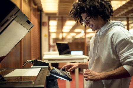 Curly-haired young man making copies on xerox in the library
