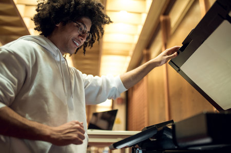 Curly-haired young man making copies on xerox in the library