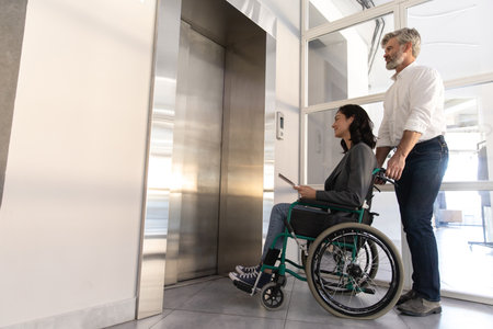 Man communicating with female in wheelchair near list in office hallの写真素材