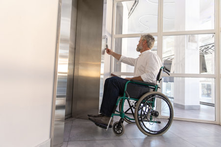 Male entrepreneur with disabilities in wheel chair waiting for elevator in officeの写真素材
