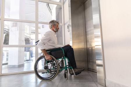 Male entrepreneur with disabilities in wheel chair waiting for elevator in office