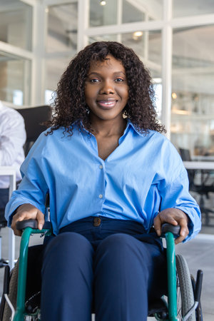 Woman in wheelchair managing her job despite her disability posing in modern officeの写真素材