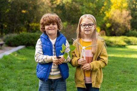 Children holding young plant and model of wind turbine symbolizing renewable energy growthの写真素材