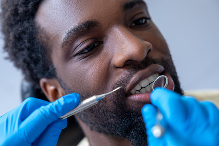 Male dentist in modern dental office examining African American patientâs teeth with mirror and dental toolsの写真素材