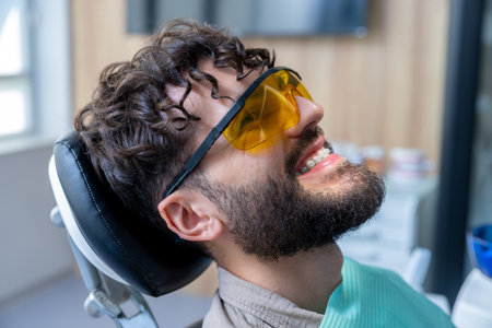 Man in protective glasses in dentist chair having teeth care proceduresの写真素材