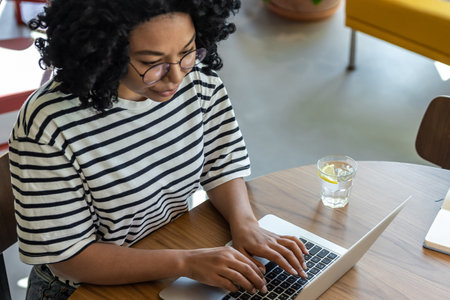 Woman in striped blouse working on laptop and having coffeeの写真素材