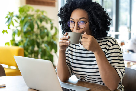 Business woman in striped blouse working on laptop and having coffeeの写真素材