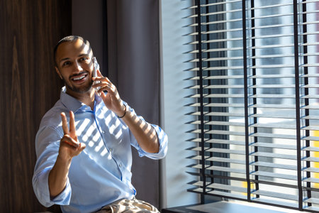 Businessman talking confidently on his mobile phone while standing near large windows in officeの写真素材