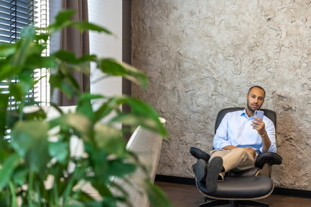 African American business man sitting in chair in office using smartphone while having breakの写真素材