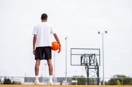 Tall man in sportswear standing with a ball in hands near the basketball playgroundの写真素材