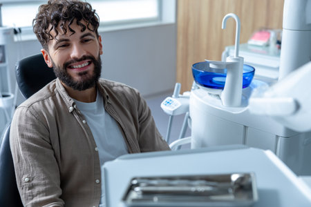 Smiling man looking at camera sitting in dental chair waiting for dental checkupの写真素材