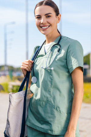 Smiling young nurse with a bag on her shoulder near the carの写真素材