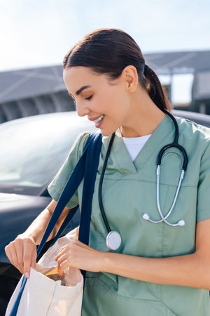Smiling young nurse with a bag on her shoulder near the carの写真素材