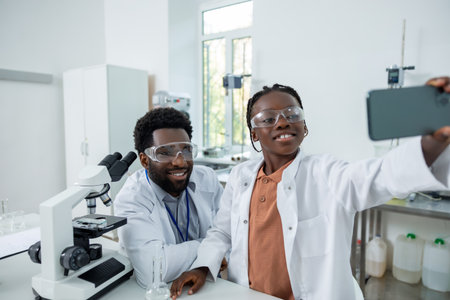 Happy teacher and student in lab coats making selfie on a phoneの写真素材
