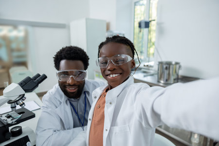 Happy teacher and student in lab coats making selfie on a phone