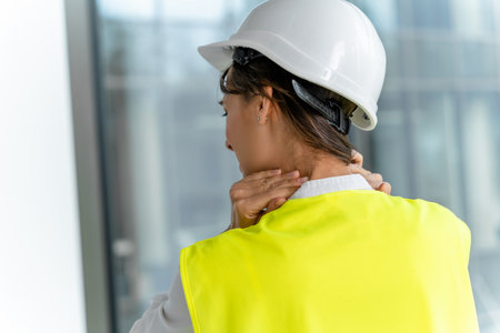 Female engineer in yellow vest suffering from pain in her neck