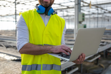 Male engineer in hardhat and protective glasses working on a laptop at a construction site