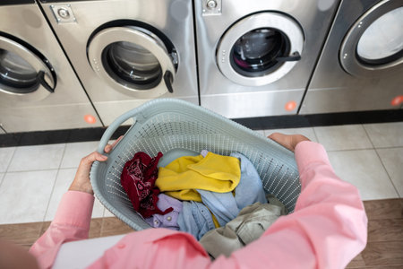 Woman in pink tshirt in a laundry room with a basket with clothes on handsの写真素材