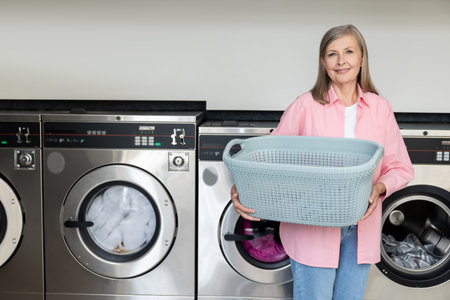 Mature caucasian woman standing near laundromat with a basket in handsの写真素材