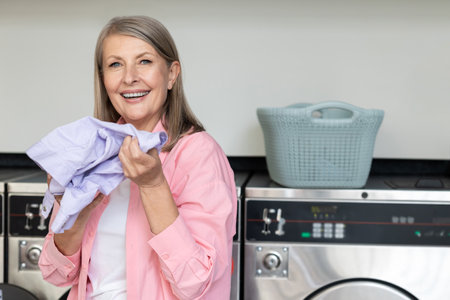 Mature caucasian woman in pink tshirt holding in hands fresh clean clothesの写真素材