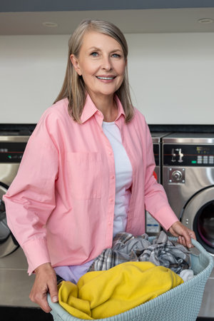 Smiling mature caucasian woman in pink tshirt carrying a basket with clothes from laundryの写真素材