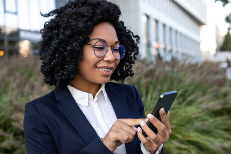 Business woman standing with a phone in hands and looking at the screenの写真素材