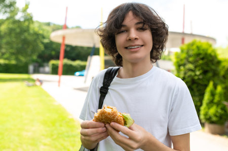 Hungry student eating burger for lunch and looking happyの写真素材