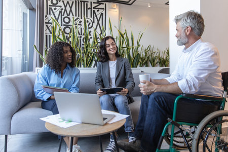 Man in wheelchair collaborating with colleagues in coworking space using laptop and internet