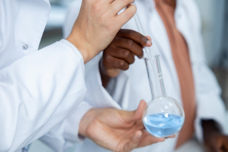Diverse medical woman and man in laboratory holding transparent flask with chemical solution