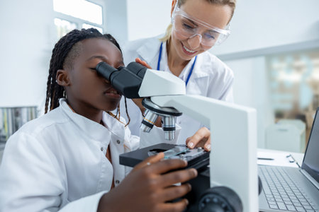 Teacher helping a student in a protective glasses to scrutinize substance in a microscope