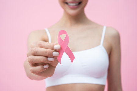 Smiling young dark-haired woman in white bra with pink ribbon in handの写真素材