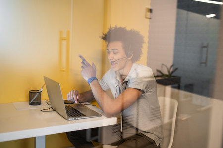 Young curly-haired man working in a call center and looking involved