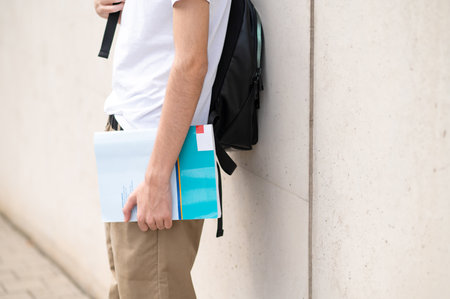 School boy in white tshirt and with a book in hand standing near the wallの写真素材