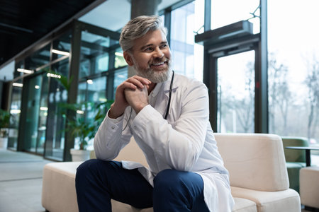 Smiling doctor in lab coat sitting on the sofa in a clinic hallの写真素材