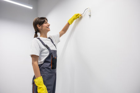 Dark-haired young woman in yellow gloves painting the wallの写真素材