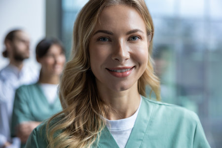 Woman doctor in medical uniform posing in clinic office hall with medical workers on backgroundの写真素材