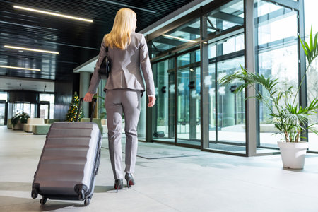 Woman in a suit carrying a big suitcase after arriving to the destinationの写真素材