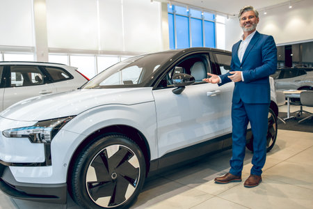 Salesman in dealership salon presenting new car to customersの写真素材